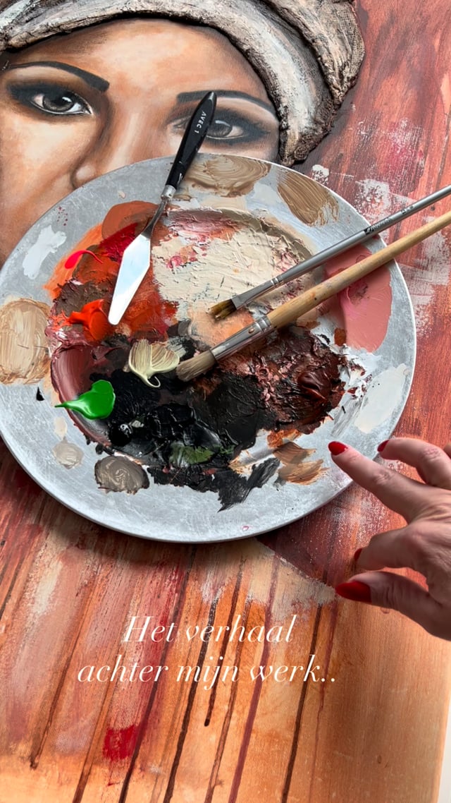 Een palet met verf, penselen en een paletmes op de werktafel, met een schilderij op de achtergrond.